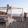 Spiaggia con sabbia scura, cartelli e persone in lontananza.