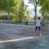 Persona che gioca a tennis su un campo all'aperto circondato da alberi.
