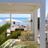 Area con sedie sotto una tettoia bianca, ombrelloni e cabine. Vista sul mare blu.