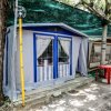 Una tenda da campeggio con finestre blu e tende a pizzo, ombreggiata da alberi.