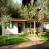 Una casetta con terrazza, sedie arancioni e tavolo su prato verde circondata da alberi.
