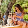 Una ragazza seduta su un muretto accarezza un piccolo cane bianco e marrone sotto un albero.