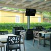 Sala all'aperto con tavoli e sedie, TV appesa e arbusti verdi all'esterno.