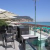 Terrazza con sedie e tavoli sotto ombrelloni, vista mare e spiaggia affollata.