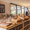 Buffet di colazione con pane, affettati, frutta e cartelli. Grandi finestre sullo sfondo.