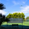 Campo da tennis con rete e cartello, alberi sullo sfondo.