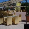 Tavoli con sedie di vimini sotto una tettoia, vasi di piante su una terrazza.