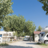 Area camper con veicoli parcheggiati, staccionata bianca e alberi frondosi.