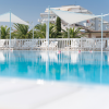 Piscina con sedie a sdraio e vele bianche, edifici sullo sfondo.