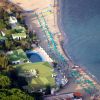 Vista aerea di una spiaggia con ombrelloni turchesi allineati vicino all'acqua, immersa nel verde.