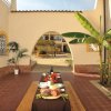 Un tavolo esterno con salumi, pane e vino. Archi, piante tropicali e cortile sullo sfondo.