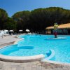 Piscina ampia con un'isola centrale colorata, circondata da ombrelloni bianchi e lettini.