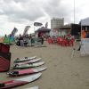 Spiaggia con tavole da surf, sedie rosse e striscioni esposti in una giornata nuvolosa.