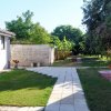 Un sentiero di piastrelle bianche in un giardino verde con muri in pietra e alberi.