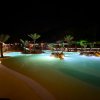 Piscina con illuminazione notturna e scivoli, palme sparse attorno.